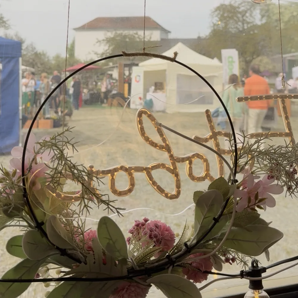 Blick durch das Fenster der Fotobox auf den Markt, davor ein Blumenkranz mit Leuchtschrift